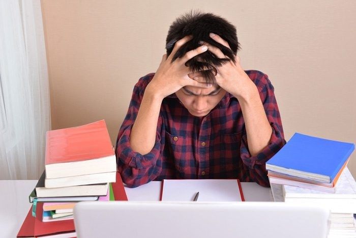 Stressad elev med händerna mot huvudet framför böcker och laptop